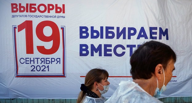 Члены местной избирательной комиссии проходят мимо предвыборной доски в первый день трехдневных парламентских выборов. Россия, 17 сентября 2021 года. Фото: RUETERS/Максим Шеметов Члены местной избирательной комиссии проходят мимо предвыборной доски в первый день трехдневных парламентских выборов. Россия, 17 сентября 2021 года. Фото: RUETERS/Максим Шеметов