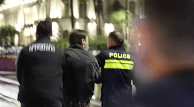 Силовики уводят задержанного на акции протеста в Тбилиси. Стоп-кадр Левана Зазадзе для Publika, https://www.facebook.com/publika.ge/videos/3195768820588730 (деятельность компании Meta, владеющей Facebook, запрещена в России).