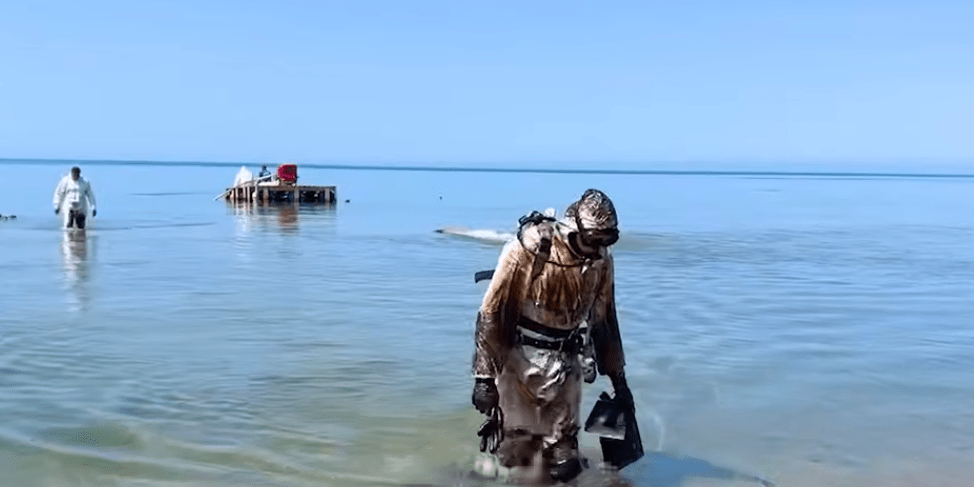 Водолаз выходит из моря после уборки мазута. Стоп-кадр видео оперштаба Краснодарского края от 07.06.25, https://t.me/opershtab23/13603.
