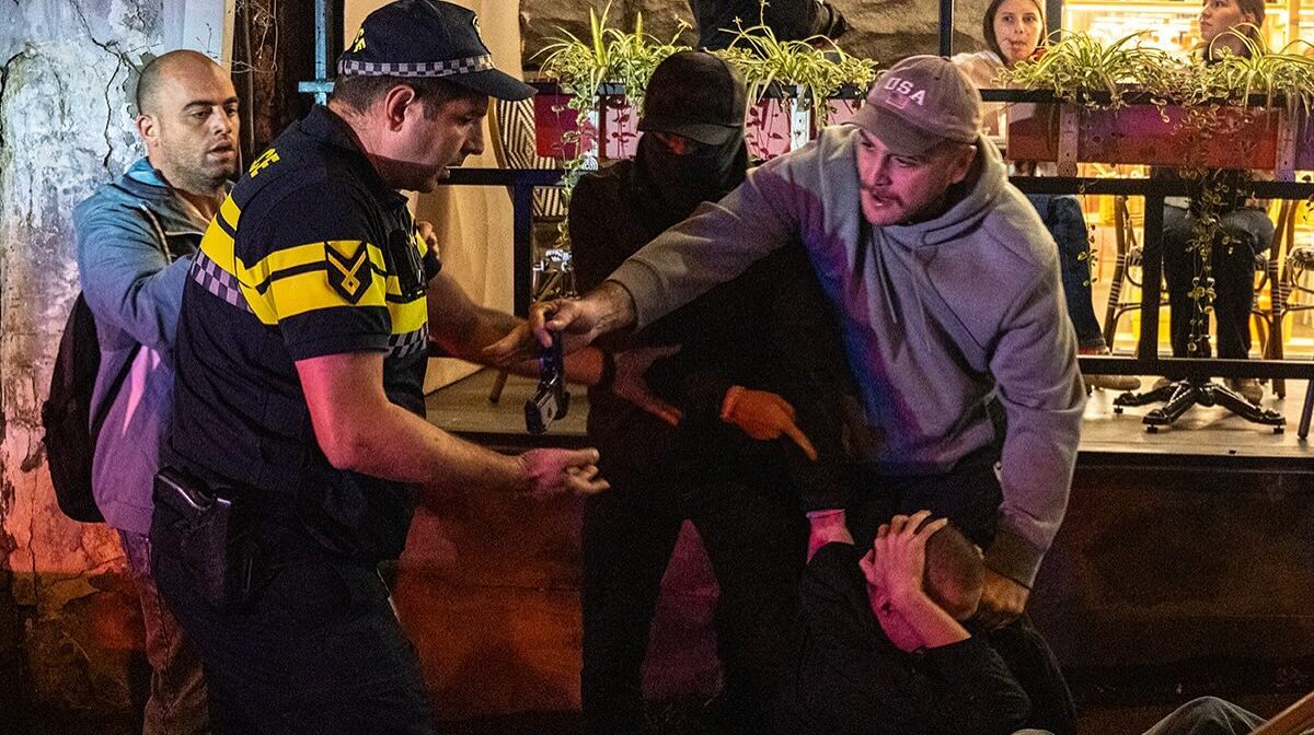 Леван Джобава (в сером свитшоте и бейсболке) передает патрульному пистолет нападавшего (держит руки за головой), 15 сентября 2025 года. Фото: Мариам Кавшбая / Publika 