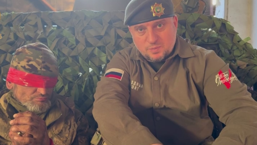 Украинский пленный с завязанными глазами и глава спецназа "Ахмат" Апти Алаудинов. Стоп-кадр видео из Telegram-канала Рамзана Кадырова от 20.04.25, https://t.me/RKadyrov_95/5668